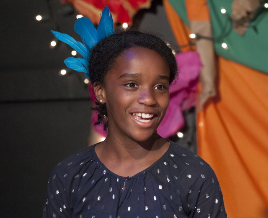 Smiling girl with blue feathers, possibly in a play or performance.