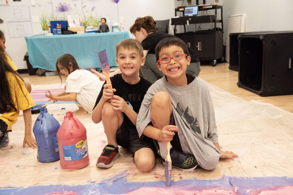 a group of kids sitting on the floor with paint on the floor