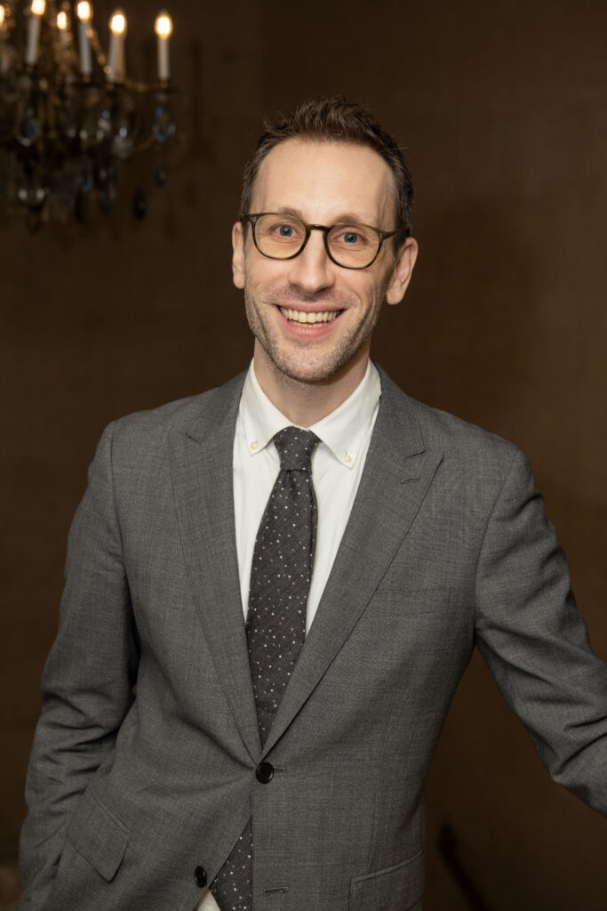 Man in suit and glasses smiling, possibly related to London Mini Intensive.