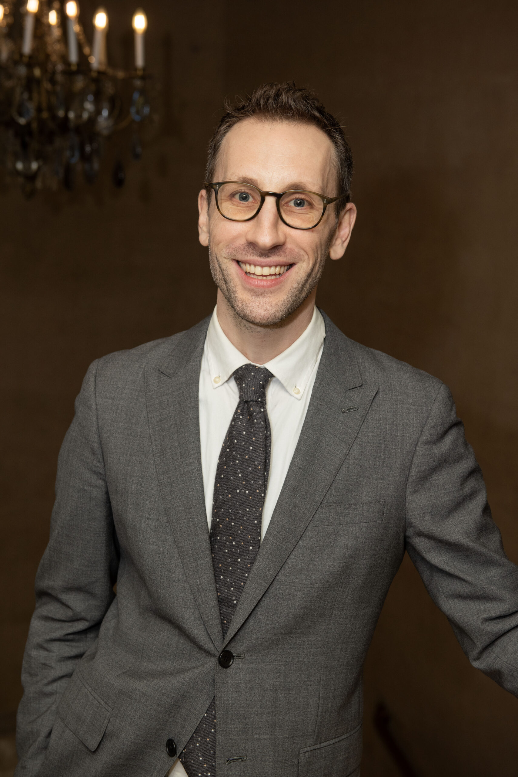 Man in suit and glasses smiling, possibly related to London Mini Intensive.