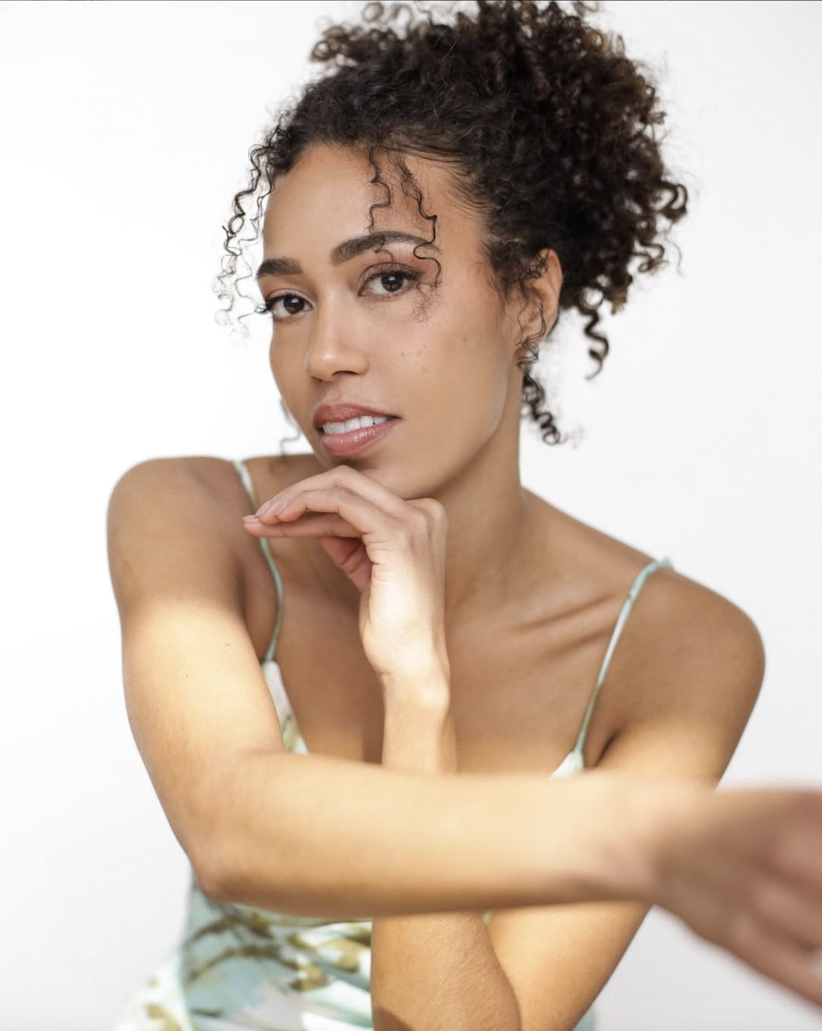 Portrait of a woman with curly hair, hand on chin, looking thoughtfully at the camera.
