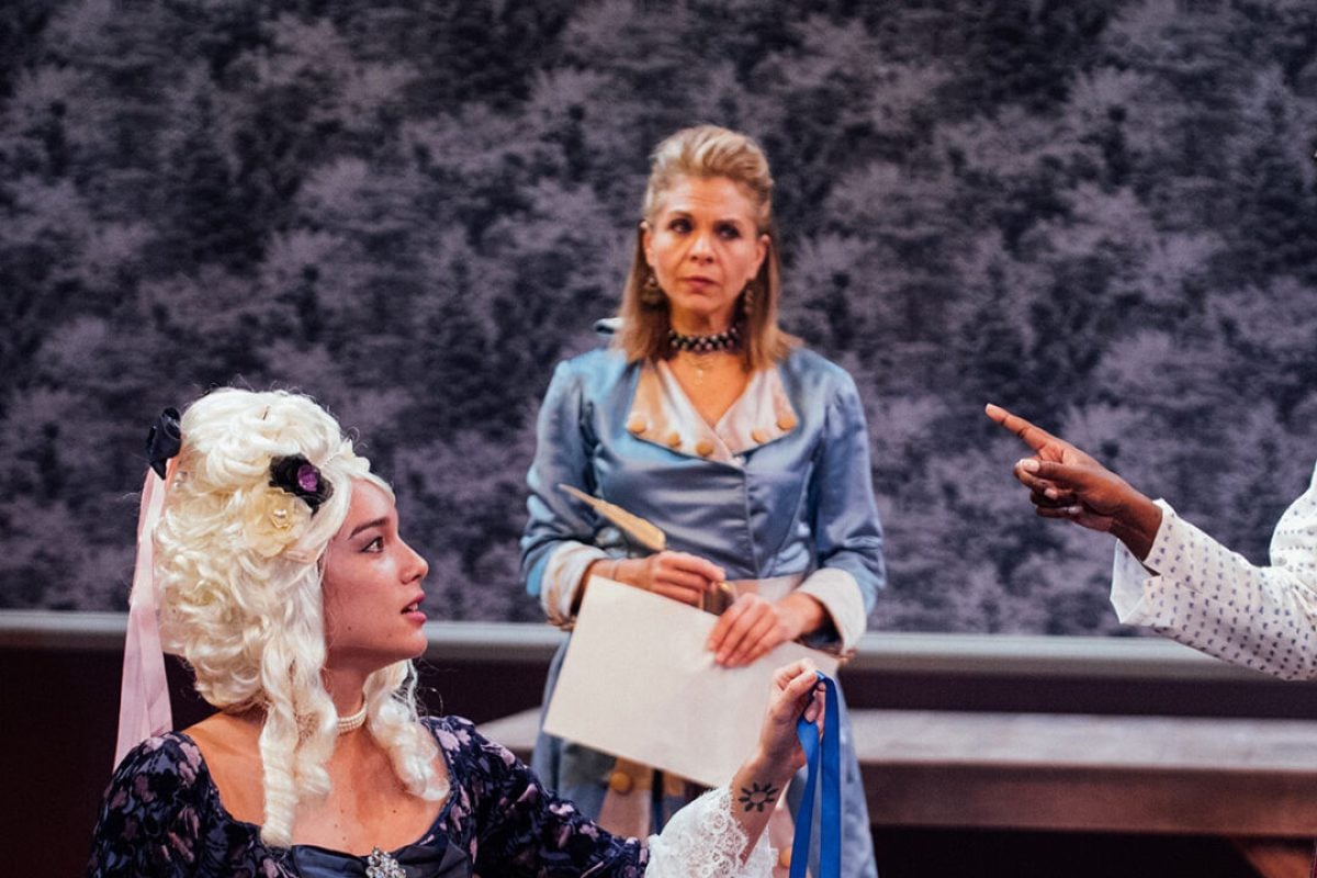 Scene from a theatrical production featuring actresses in period costumes.