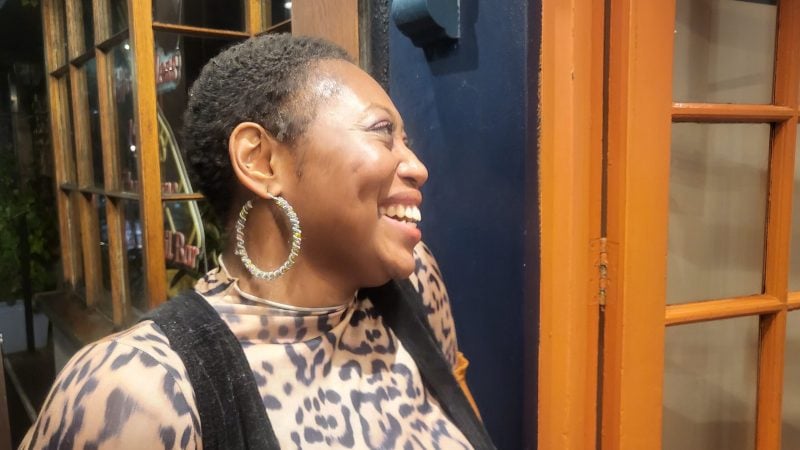 Smiling Black woman with short hair and hoop earrings, wearing animal print.