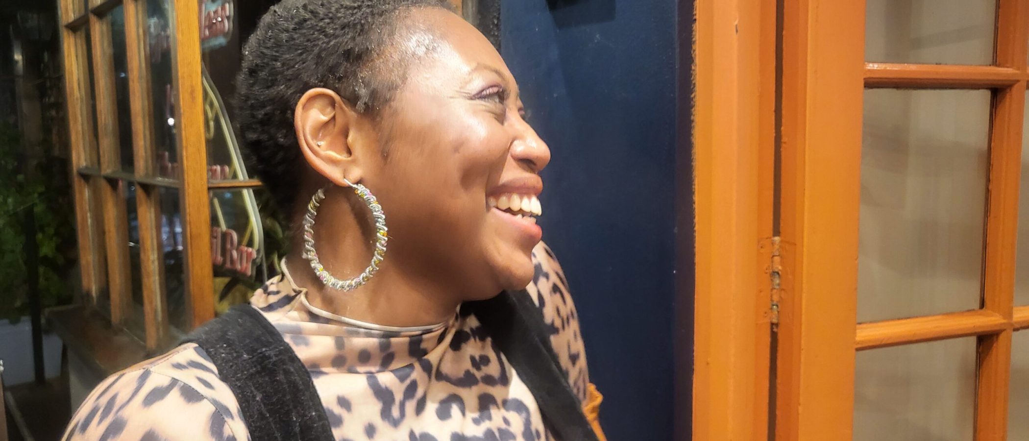 Smiling Black woman with short hair and hoop earrings, wearing animal print.