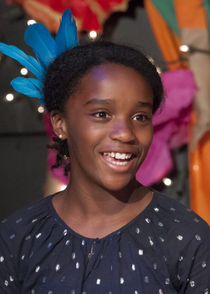 Smiling girl with blue feathers, possibly in a play or performance.