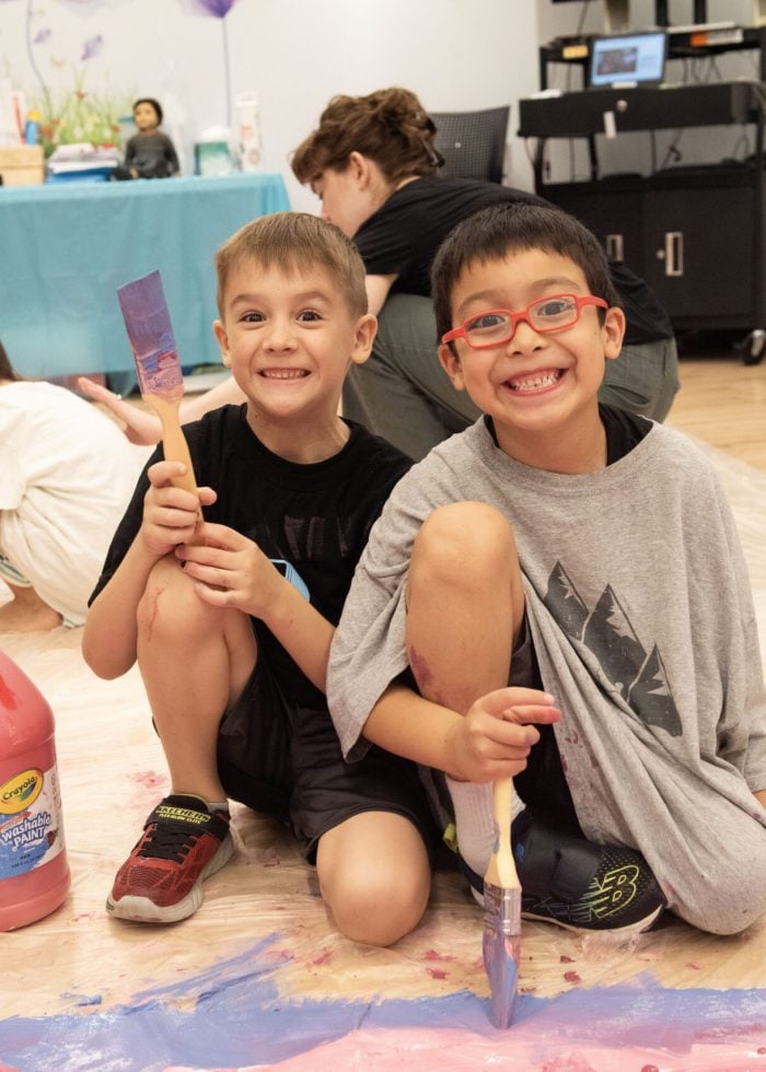 a group of kids sitting on the floor with paint on the floor
