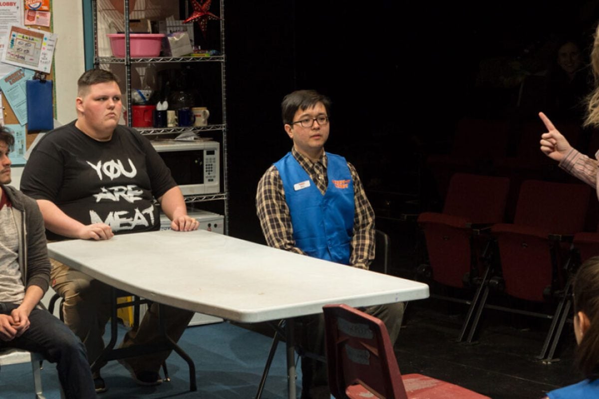 Theater production scene with actors around a table.