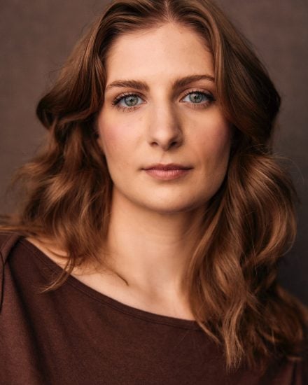 Headshot of Madeline Keplinger with wavy brown hair and striking blue eyes.