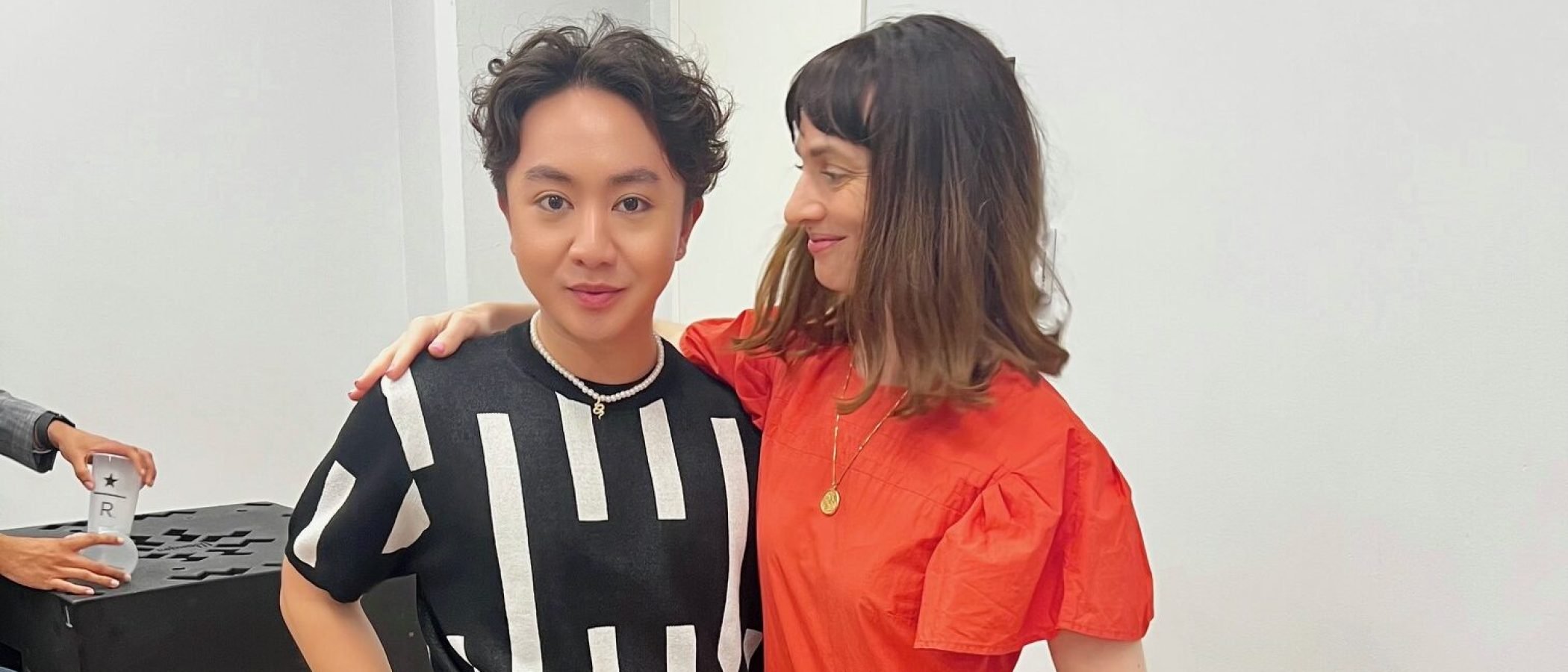 Two people posing indoors, one in red dress, one in black and white top.
