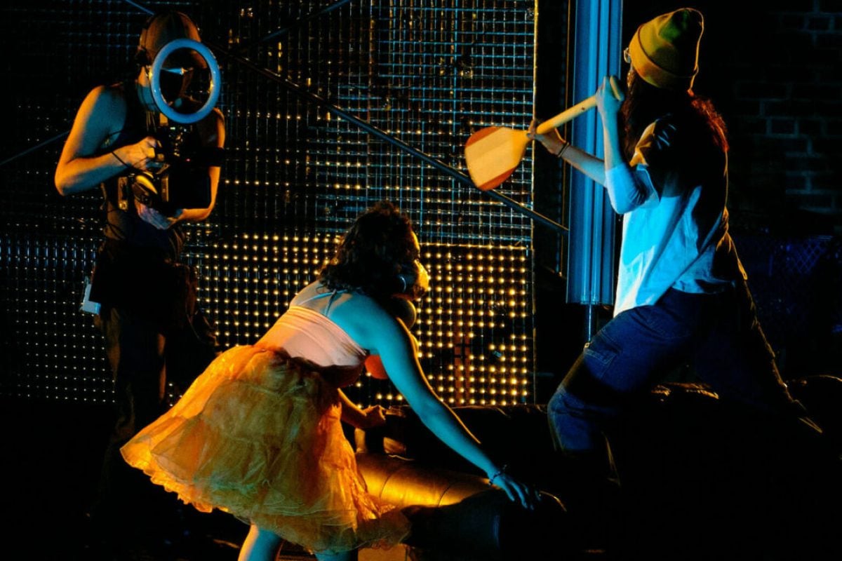 Stage production scene with actors in costume and dramatic lighting.