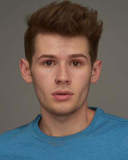Portrait of a young man with a nose ring and stylish brown hair.