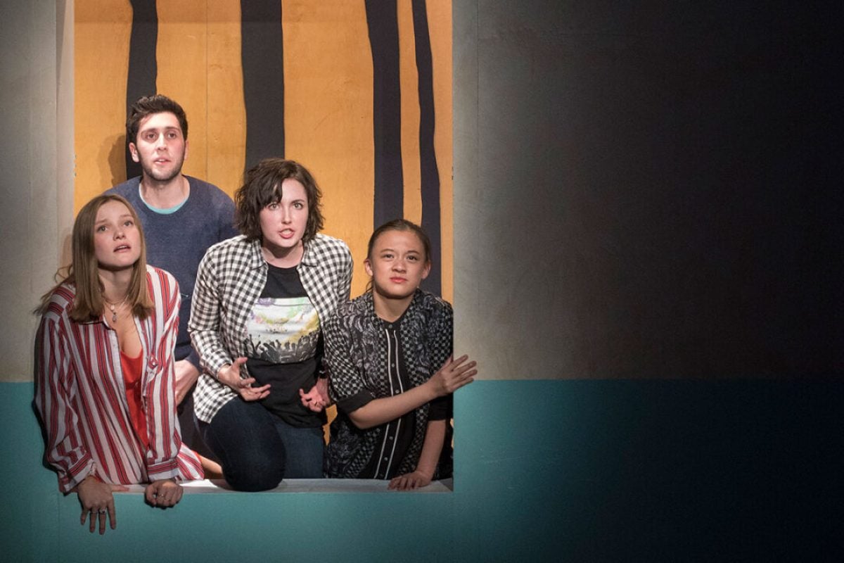 Four actors in a theatrical production look out from a window, expressions of surprise or concern.